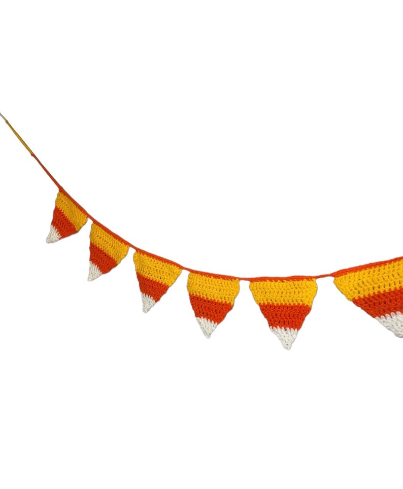 May include: A crocheted banner featuring triangular pennants in the colors of candy corn: white, yellow, and orange. The pennants are strung together on a thin orange cord, creating a festive decoration.