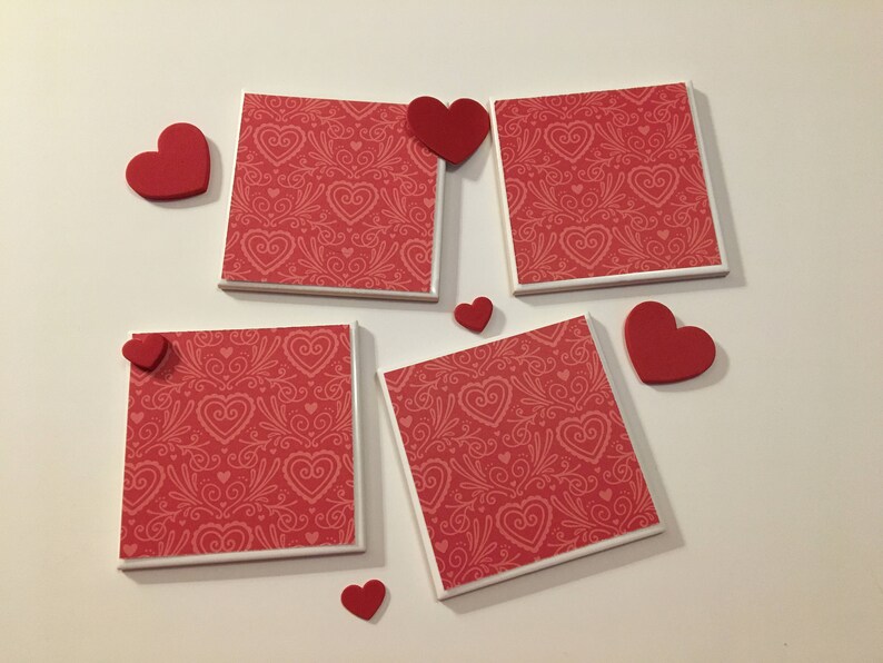 May include: Five red and white ceramic coasters with a heart pattern. Each coaster has a small red heart attached to the top.