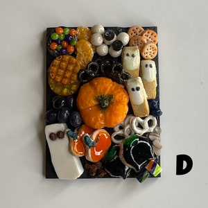 Op de afbeelding: Een Halloween-charcuteriebord met een verscheidenheid aan snacks, waaronder een pompoen, pretzelsticks, kaas en snoep. Het bord is versierd met zwarte en witte spookvormen en verschillende andere Halloween-decoraties.