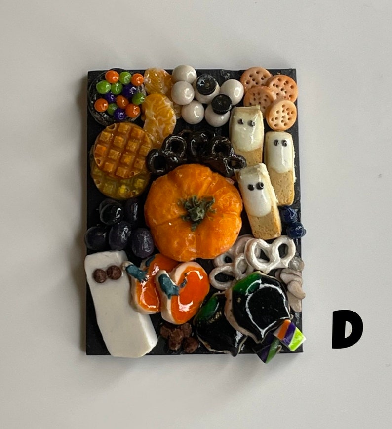 Op de afbeelding: Een Halloween-charcuteriebord met een verscheidenheid aan snacks, waaronder een pompoen, pretzelsticks, kaas en snoep. Het bord is versierd met zwarte en witte spookvormen en verschillende andere Halloween-decoraties.