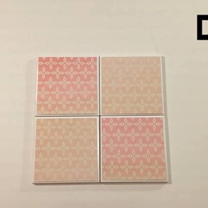 K&ouml;nnte beinhalten: Satz mit vier quadratischen Untersetzern mit einem geometrischen Muster in Rosa und Wei&szlig;. Die Untersetzer haben einen wei&szlig;en Rand.