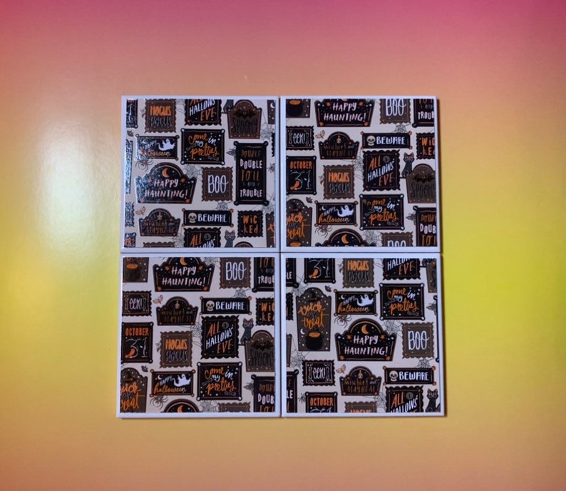 Pu&ograve; includere: Un set di quattro sottobicchieri quadrati con un motivo ripetitivo a tema Halloween. Il design presenta cornici rettangolari nere con testo arancione e bianco come Happy Haunting, Boo, Beware e Hocus Pocus su sfondo chiaro.