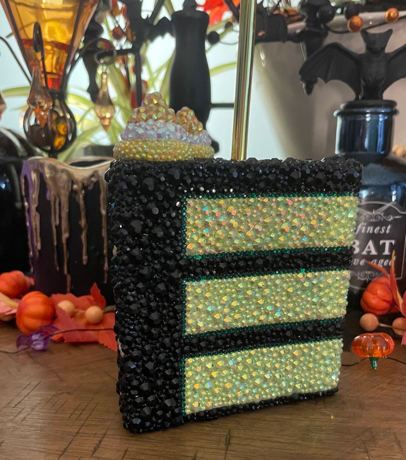 May include: A black and green layered cake with a white and iridescent topper. The cake is covered in rhinestones and has a green border around each layer.