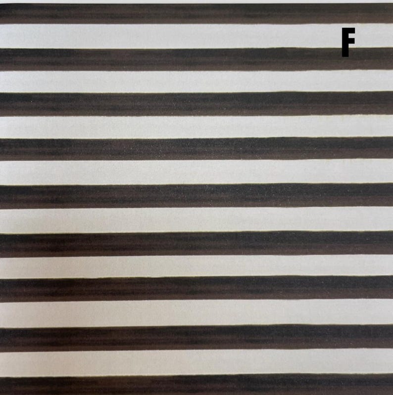 K&ouml;nnte beinhalten: Eine Stoff- oder Papieroberfl&auml;che mit einem sich wiederholenden Muster aus horizontalen dunkelbraunen Streifen, die sich mit cremewei&szlig;en Streifen abwechseln. Der Buchstabe F ist in Schwarz in der oberen rechten Ecke des Streifenmusters aufgedruckt.
