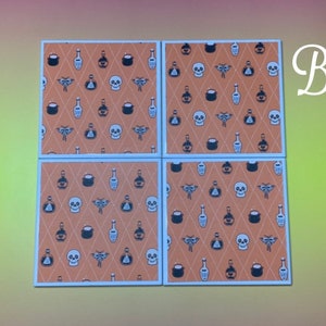Puede incluir: Cuatro posavasos cuadrados con un patr&oacute;n repetido de calaveras, botellas de pociones y otros iconos tem&aacute;ticos de Halloween sobre un fondo de diamantes naranja. Los posavasos tienen bordes blancos.
