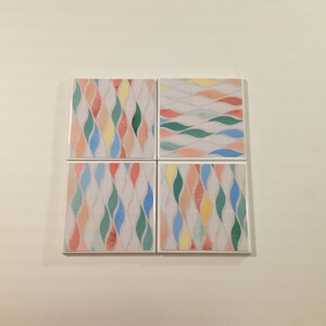 K&ouml;nnte beinhalten: Set aus vier quadratischen Untersetzern mit einem farbenfrohen abstrakten Muster aus wellenf&ouml;rmigen Linien in den Farben Rosa, Blau, Gr&uuml;n und Gelb auf wei&szlig;em Hintergrund.