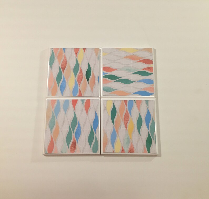 K&ouml;nnte beinhalten: Set aus vier quadratischen Untersetzern mit einem farbenfrohen abstrakten Muster aus wellenf&ouml;rmigen Linien in den Farben Rosa, Blau, Gr&uuml;n und Gelb auf wei&szlig;em Hintergrund.