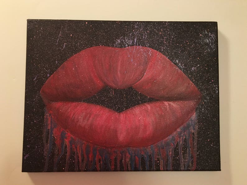 Pu&ograve; includere: Primo piano di un'impronta di labbra dipinte di rosso su uno sfondo di tela nero con effetto splatter. L'impronta di labbra cola di vernice rossa e blu.