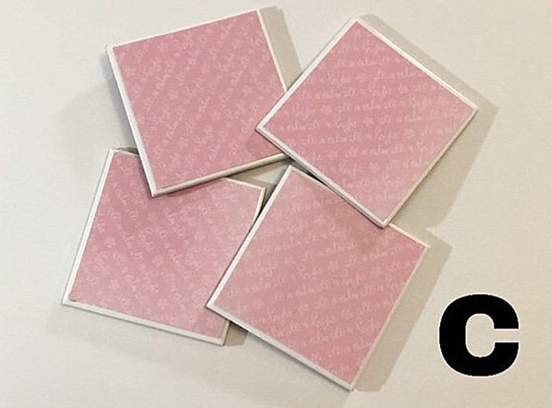 May include: Four pink square coasters with a white script pattern. The coasters are stacked on top of each other.