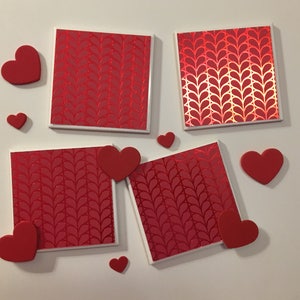 May include: Four red square coasters with a white border and a repeating pattern of red hearts. The coasters are surrounded by red hearts of various sizes.