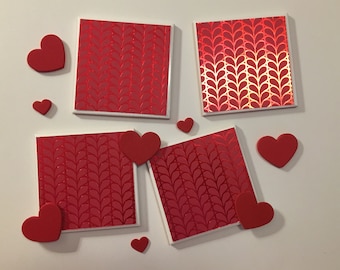 May include: Four red square coasters with a white border and a repeating pattern of red hearts. The coasters are surrounded by red hearts of various sizes.
