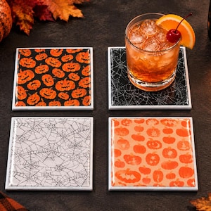 May include: A set of four square coasters featuring Halloween-themed designs. Two coasters display orange jack-o'-lantern patterns on black and light orange backgrounds, while the other two feature intricate black and white spiderweb patterns.