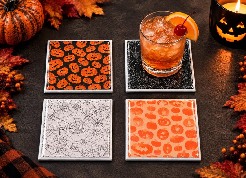 May include: A set of four square coasters featuring Halloween-themed designs. Two coasters display orange jack-o'-lantern patterns on black and light orange backgrounds, while the other two feature intricate black and white spiderweb patterns.