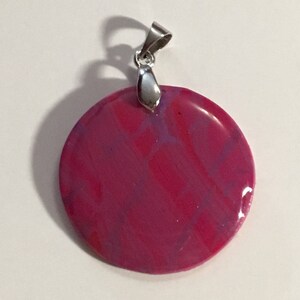 Puede incluir: Un colgante redondo con un dise&ntilde;o marmoleado rosa y morado y una argolla plateada.