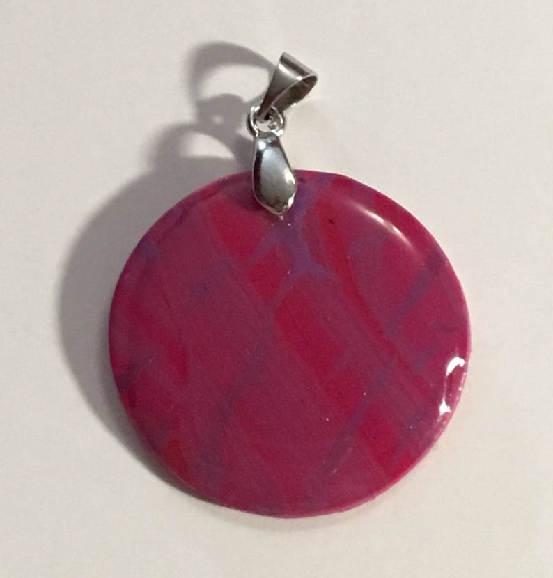 Puede incluir: Un colgante redondo con un dise&ntilde;o marmoleado rosa y morado y una argolla plateada.
