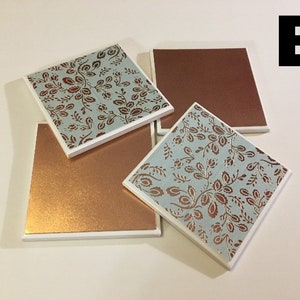 Puede incluir: Cuatro posavasos cuadrados con borde blanco. Dos posavasos presentan un patr&oacute;n floral azul y cobre. Dos posavasos son de cobre s&oacute;lido.