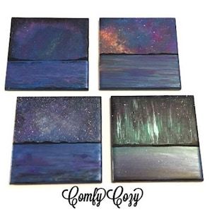 Puede incluir: Conjunto de cuatro pinturas cuadradas sobre lienzo que representan diferentes escenas de cielo nocturno. Cada pintura presenta una escena de agua azul oscuro con una l&iacute;nea de horizonte negra y un cielo nocturno colorido arriba. Los cielos presentan una galaxia, estrellas y la aurora boreal.