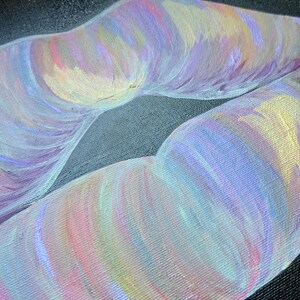 May include: A painting on a textured black canvas depicting a pair of lips rendered in iridescent brushstrokes of pastel pink, lavender, light blue, and soft yellow. The artwork features visible paint texture and a vibrant, multi-colored finish.
