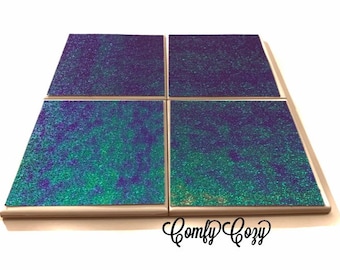 May include: Set of four square coasters with a iridescent green and purple glitter finish. The coasters have a light wood frame and are arranged in a 2x2 grid. The text "Comfy Cozy" is visible in the bottom right corner of the image.