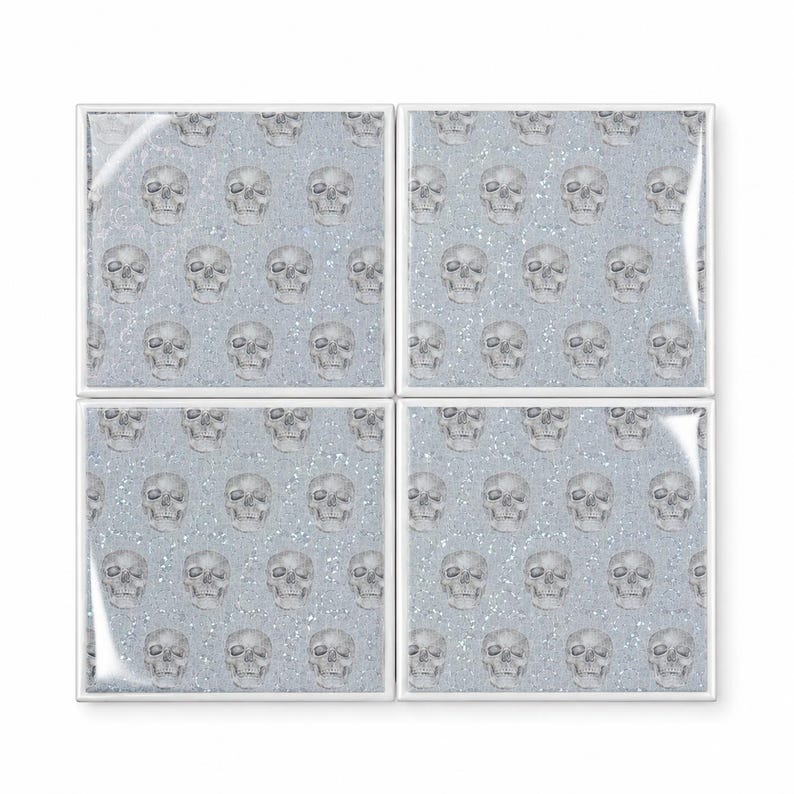 Peut inclure: Un ensemble de quatre dessous de verre carr&eacute;s pr&eacute;sentant un motif r&eacute;p&eacute;titif de cr&acirc;nes humains gris imprim&eacute;s sur un fond bleu clair avec une texture scintillante et paillet&eacute;e. Chaque dessous de verre a une bordure blanche nette.