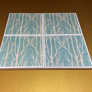 May include: Set of four square ceramic coasters with a white tree branch design on a light blue background.