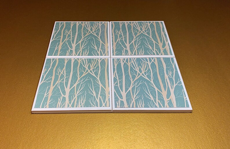 May include: Set of four square ceramic coasters with a white tree branch design on a light blue background.