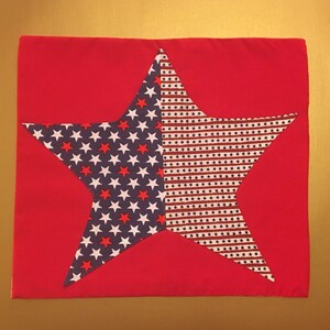Peut inclure: Un coussin en tissu rouge avec une grande &eacute;toile blanche et bleue au centre. L'&eacute;toile est faite de tissu avec un motif de petites &eacute;toiles blanches sur fond bleu et de rayures rouges et blanches sur fond bleu.