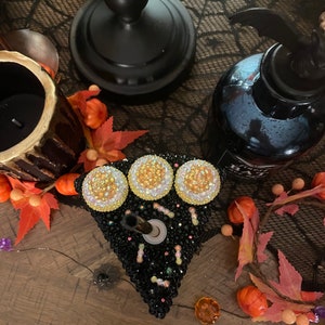 May include: A black and white cake-shaped candle holder with three yellow and white rhinestones on top. The candle holder is decorated with black and white rhinestones and small black and white sprinkles.