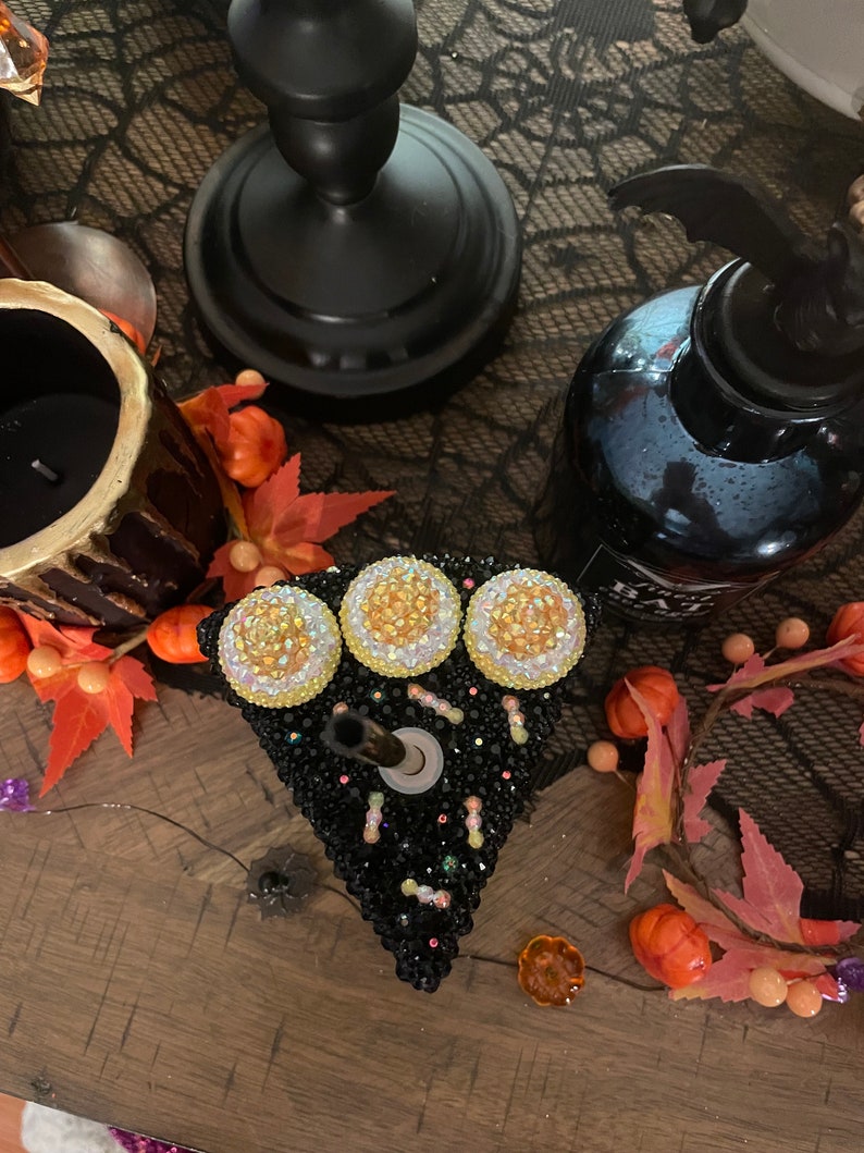 May include: A black and white cake-shaped candle holder with three yellow and white rhinestones on top. The candle holder is decorated with black and white rhinestones and small black and white sprinkles.