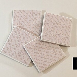 May include: Four square white coasters with a pink floral pattern and the text "It's a little bit of magic" repeated on each coaster.
