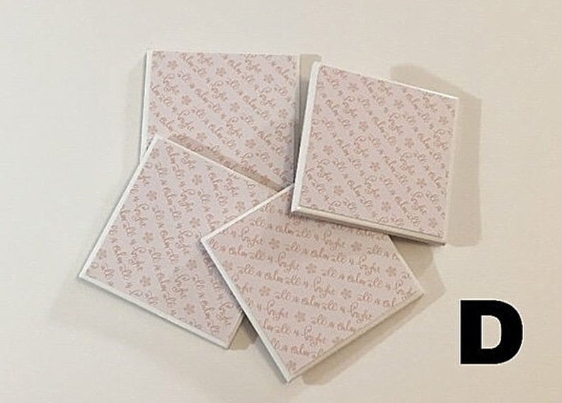 May include: Four square white coasters with a pink floral pattern and the text "It's a little bit of magic" repeated on each coaster.
