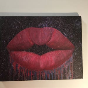 Pu&ograve; includere: Primo piano di un'impronta di labbra dipinte di rosso su uno sfondo di tela nero con schizzi di vernice blu e viola. L'impronta delle labbra cola di vernice rossa e blu.