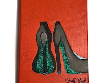 May include: A painting of two black high-heeled shoes with green glitter on an orange background. The painting is signed "Comfy Cozy".