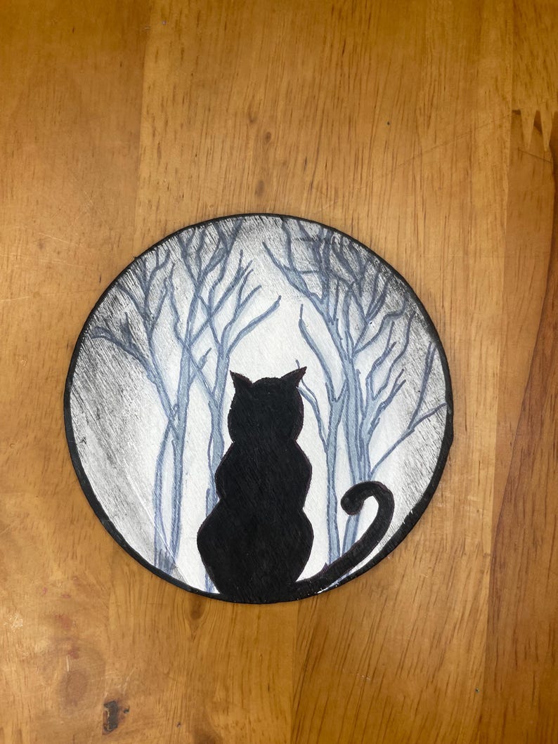 Pode incluir: Ilustra&ccedil;&atilde;o redonda a preto e branco com a silhueta de um gato preto em frente a uma cena de floresta. O gato est&aacute; de costas, com a cauda enrolada. O fundo mostra &aacute;rvores nuas numa paleta de cinza e branco nebuloso.