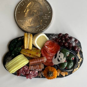 Op de afbeelding: Een miniatuur Halloween-kaas- en charcuteriebord met een spookvormige koekjesuitsteker, olijven, druiven, salami, kaas en pompoenvormige crackers.
