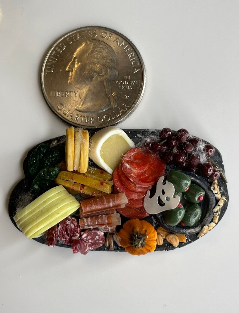 Op de afbeelding: Een miniatuur Halloween-kaas- en charcuteriebord met een spookvormige koekjesuitsteker, olijven, druiven, salami, kaas en pompoenvormige crackers.