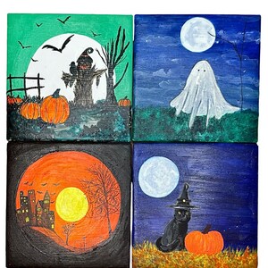 Op de afbeelding: Vier vierkante schilderijen met Halloween-thema. E&eacute;n toont een vogelverschrikker, pompoenen en een volle maan. Een andere toont een spook onder een volle maan. Een derde toont een spookhuis met een volle maan. De laatste toont een zwarte kat met een heksenhoed en een pompoen.