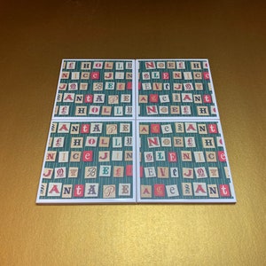 May include: Four square ceramic coasters with a green and white striped background. Each coaster features a repeating pattern of red, white, and green letters spelling out Christmas words like "Holly", "Nice", "Joy", "Bell", "Peace", "Noel", "Eve", "Santa", and "Age".