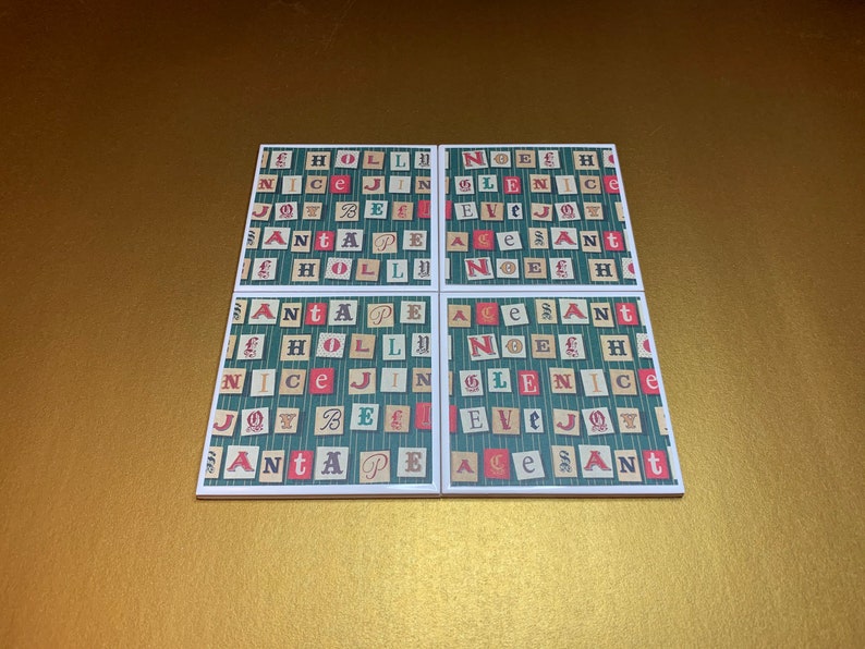May include: Four square ceramic coasters with a green and white striped background. Each coaster features a repeating pattern of red, white, and green letters spelling out Christmas words like "Holly", "Nice", "Joy", "Bell", "Peace", "Noel", "Eve", "Santa", and "Age".