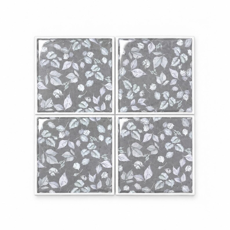Peut inclure: Un ensemble de quatre dessous de verre carr&eacute;s dispos&eacute;s en grille, chacun pr&eacute;sentant un fond gris fonc&eacute; avec un motif r&eacute;p&eacute;titif de feuilles botaniques et de petits bourgeons gris clair et blancs, le tout encadr&eacute; par un fin bord blanc.