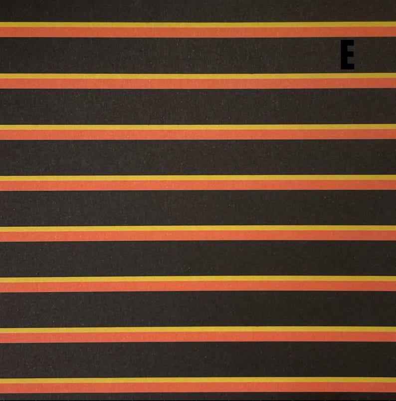 K&ouml;nnte beinhalten: Eine gemusterte Oberfl&auml;che mit sich wiederholenden horizontalen Streifen in Schwarz, Orange und Gelb. Das Design besteht aus breiten schwarzen B&auml;ndern, die durch d&uuml;nnere orange und gelbe Linien getrennt sind. Der Gro&szlig;buchstabe E ist oben rechts zu sehen.