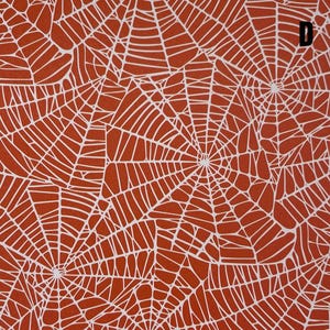 K&ouml;nnte beinhalten: Eine flache Stoffoberfl&auml;che mit einem sich wiederholenden Muster aus wei&szlig;en Spinnennetzen auf einem einfarbigen, gebrannten orangefarbenen Hintergrund. Das Design umfasst mehrere &uuml;berlappende Netzstrukturen und der Buchstabe D ist in der oberen rechten Ecke aufgedruckt.