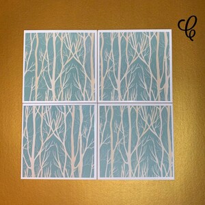 May include: Set of four square coasters with a white tree branch design on a light blue background.