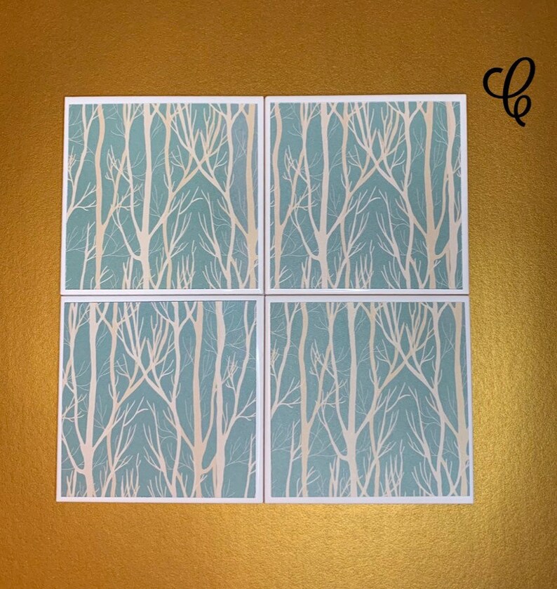 May include: Set of four square coasters with a white tree branch design on a light blue background.