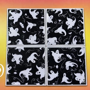 May include: A set of four square coasters featuring a repeating pattern of white ghosts and small bats on a black background. Each coaster has a glossy finish and a white border. The letter D is visible in white on the bottom left corner.