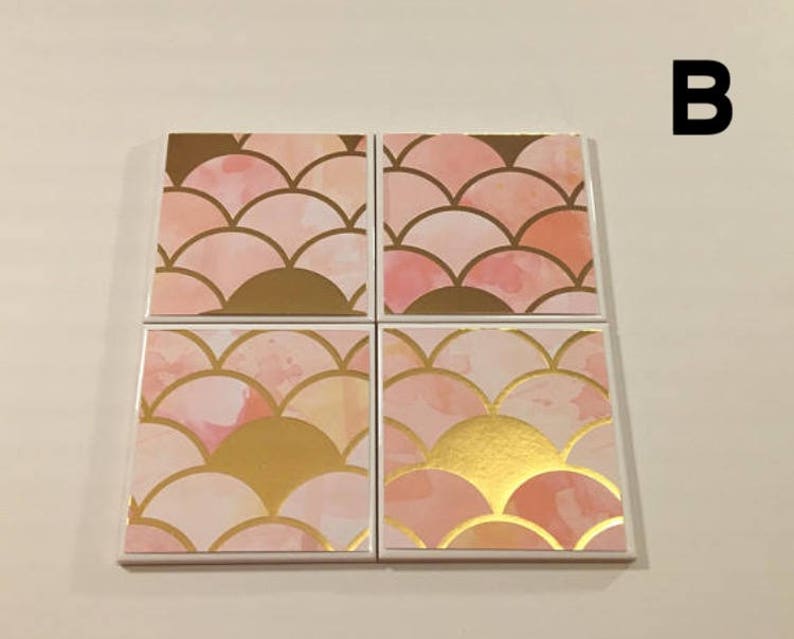 K&ouml;nnte beinhalten: Set mit vier Untersetzern in Rosa und Gold mit geometrischem Muster. Die Untersetzer zeigen ein sich wiederholendes Muster aus &uuml;berlappenden Halbkreisen in einem hellrosa und goldenen Farbschema.