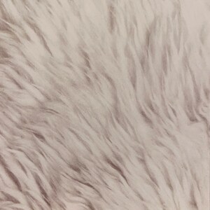 May include: A close-up of a white faux fur rug with a soft, fluffy texture.