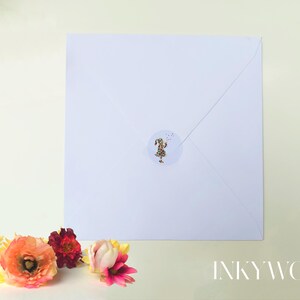May include: A white square envelope sealed with a round sticker featuring gold flecks. The envelope is surrounded by colorful flowers in shades of orange, red, and pink. The text "INKYWOOL" is visible in the bottom right corner.