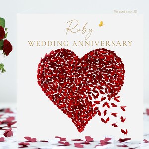 May include: A white Ruby Wedding Anniversary card featuring a heart made of red butterflies. Gold script reads "Ruby WEDDING ANNIVERSARY". A bouquet of white lilies and red roses is in the background, with scattered confetti.