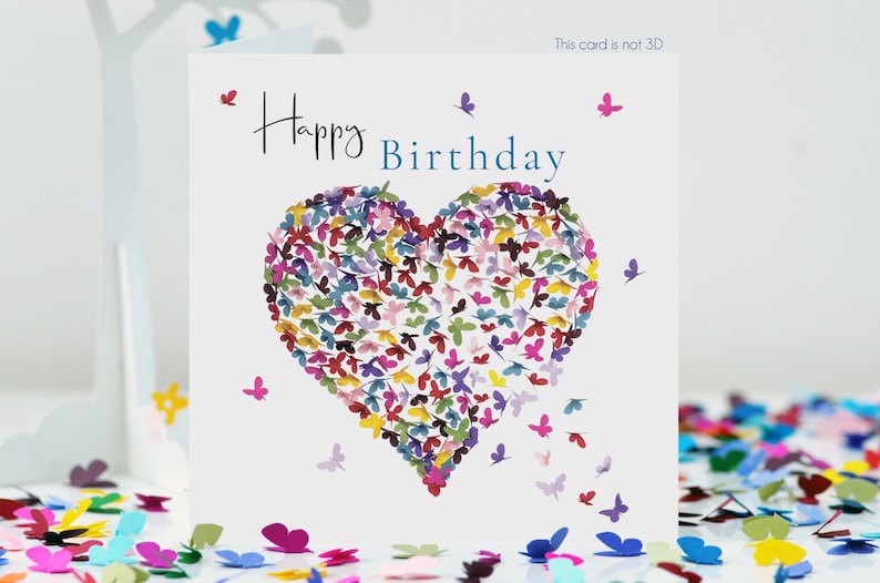 May include: A white birthday card with the words "Happy Birthday" in black and blue. A heart made of colorful butterfly cutouts is the central design, with additional butterflies scattered around the card. The text "This card is not 3D" is in the top right corner.